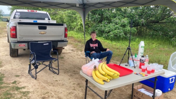 Volunteer sitting under a tent at a table with bananas and sports drinks
